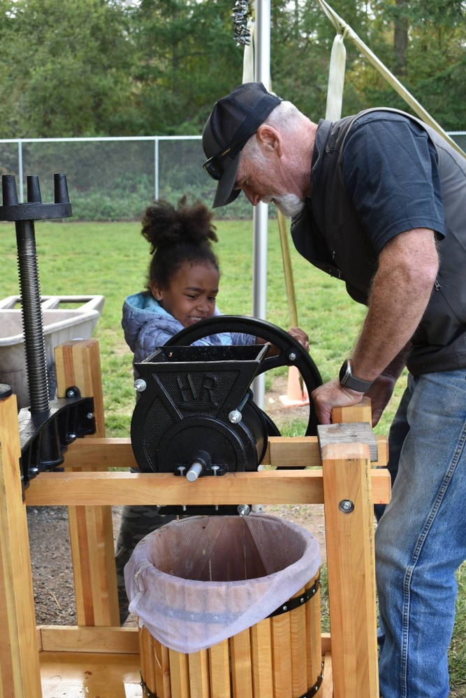 girl turning a cider press with all of her might