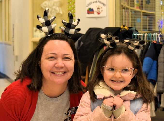 A woman and a young girl smile for the camera, both wearing festive reindeer antlers.