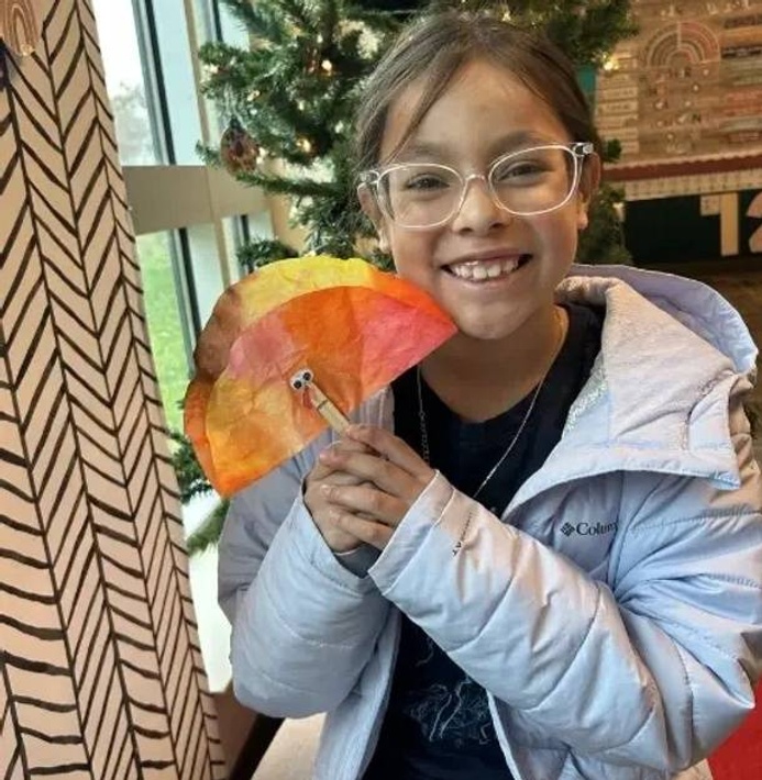 A girl smiles with her handmade coffee filter turkey art