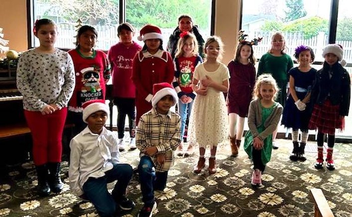 A group of children dressed in festive attire pose for a photo, some wearing Santa hats.