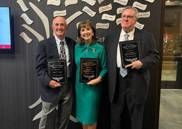 This year's inductees stand together before the Hall of Fame memorial wall in the JHS Performing Arts center, each holding plaques bearing their name. The two gentlemen, Kyle Craig and Mitch Stinnett, are in suits, flanking Glenda Austin, who wears a kelly-green dress.