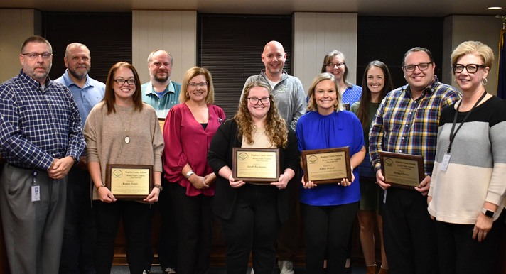 About 12 people smile for photo with at least 4 holding plaques.