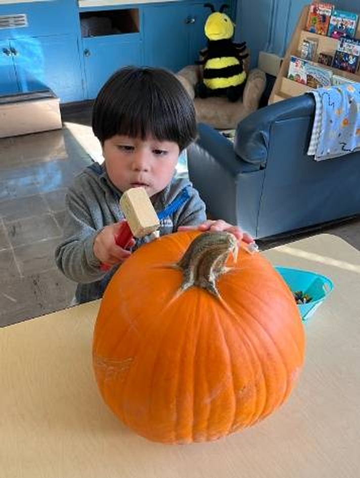 preschooler hammering into pumpkin