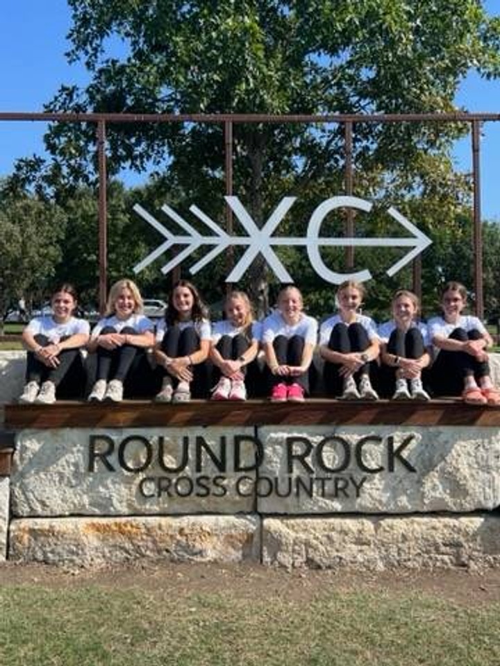 A group of girls siting for a picture on the Round Rock Cross Country course sign.