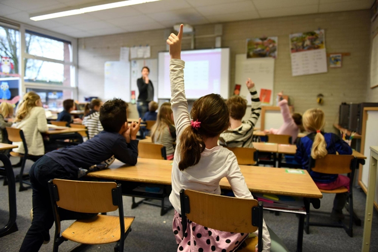 A classroom of students, with one girl raising her hand to answer a question.