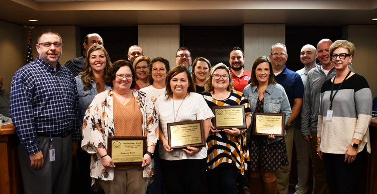 About 17 people smile for photo, with at least 4 holding plaques.