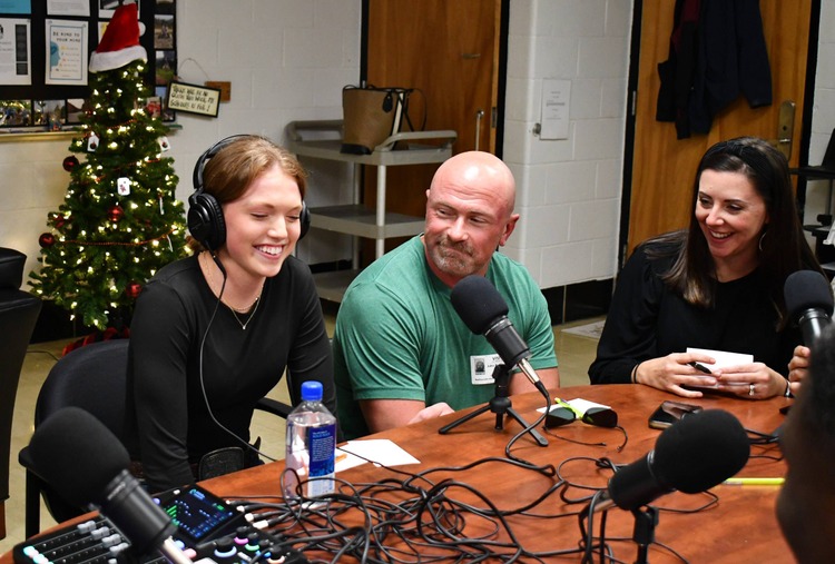 3 people sit at table with recording equipment.