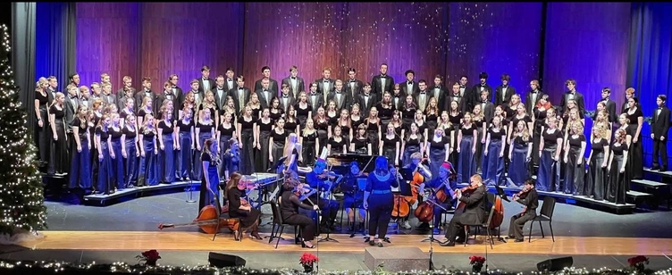 A large choir performs on stage with a string quartet and a pianist.