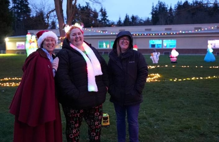 Three friends pose for a photo in front of a building decorated with Christmas lights.