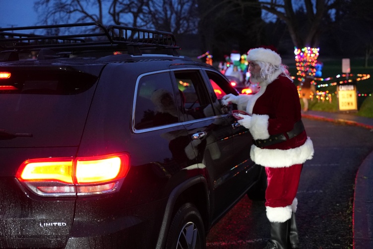 Santa Claus hands a gift to a person in a car at a holiday event.