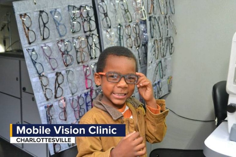 Student trying on eyeglasses with the TV caption "Mobile Vision Clinic" Charlottesville