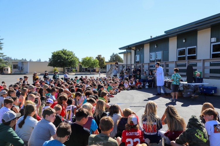 A group of students sit outside watching a science presentation