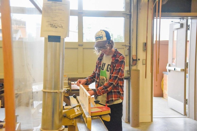 high school student cutting wood plank