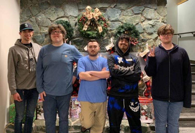 Five young men stand in front of a stone fireplace decorated with Christmas wreaths and stockings.