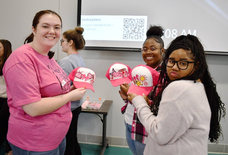 3 people hold up pink and white hats