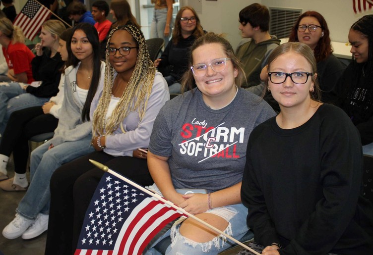 4 people sit in row, with 1 holding U.S. flag