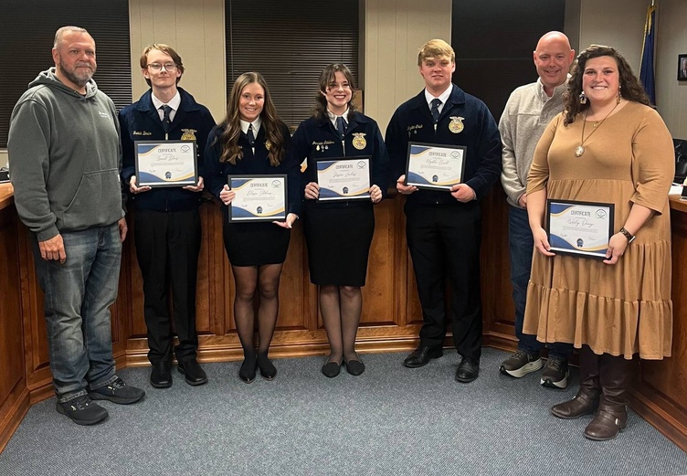 7 people stand in a row to pose for photo, with 5 holding framed certificates