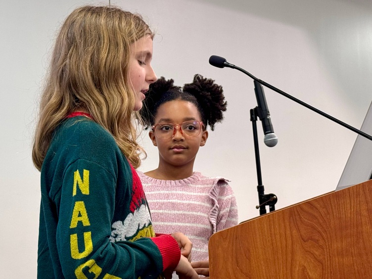 Two young girls stand at a podium presenting.