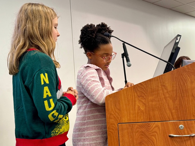 Two young girls stand at a podium presenting.