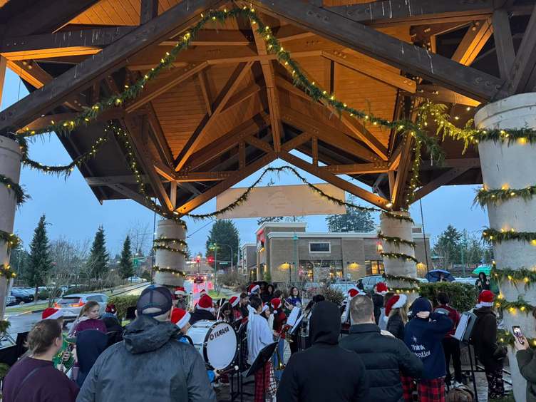 A group of student musicians perform under a festive canopy decorated with lights and greenery.