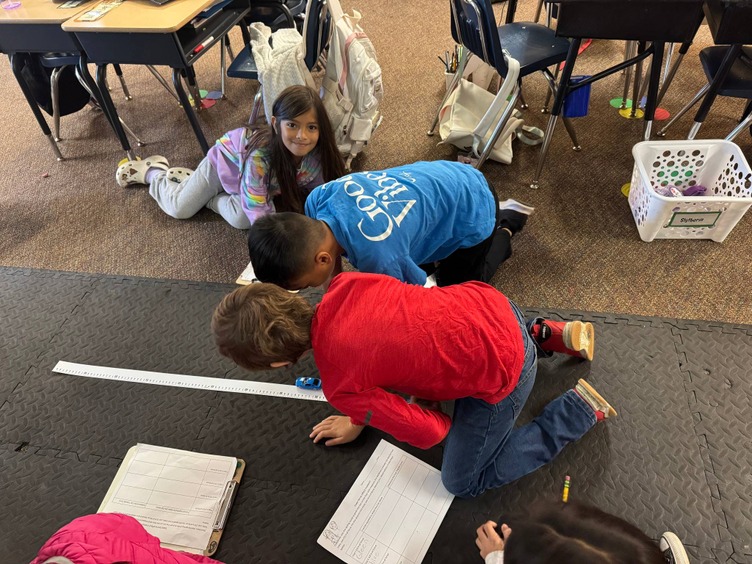 elementary students using spring scale with cars