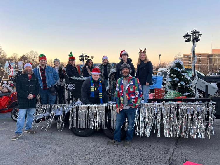 About 10 people pose on and next to float with silver fringe and a lamppost