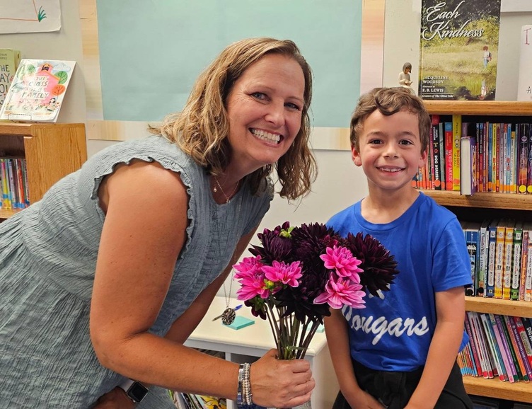 Photo of teacher holding bouquet of chrysanthemums standing nest to student.