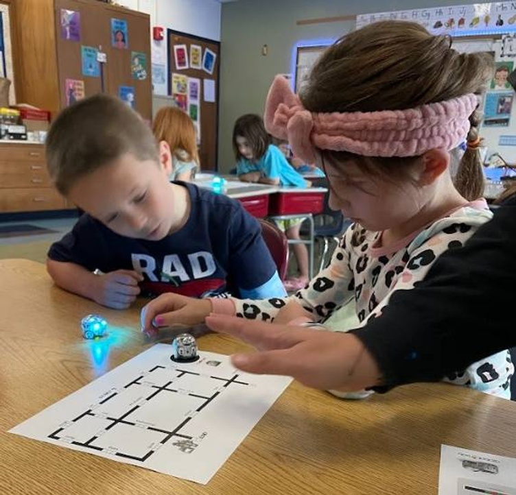 Two first grade students sitting at a student desk calibrating an ozobot.