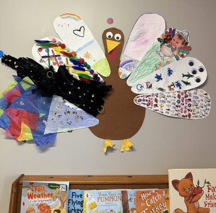 In a preschool classroom, there is a construction paper turkey on the wall, and each tail feather was artfully decorated by one student, for a diverse variety of joyful tail feathers.