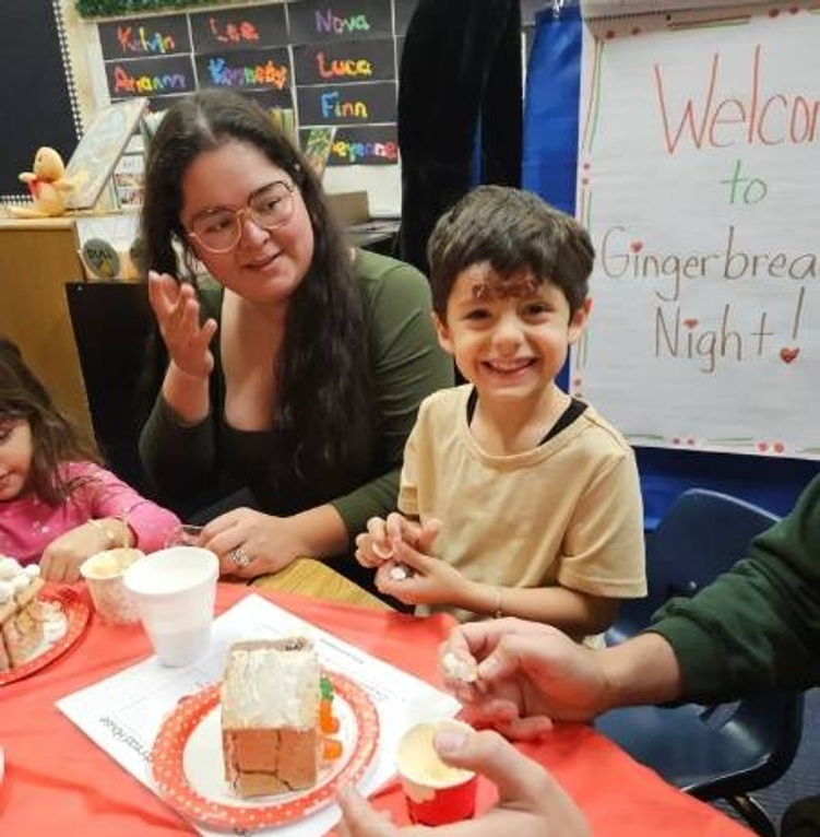 A young boy smiles as he decorates a gingerbread house at a 'Gingerbread Night' event.