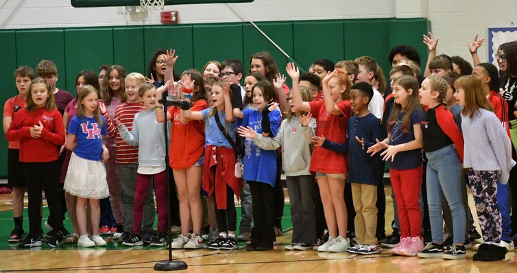 About 30 kids sing together in a school choir in the gym