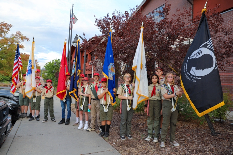 A group of students pose for a photo in their scout uniforms, holding the flags for the presentation of colors.