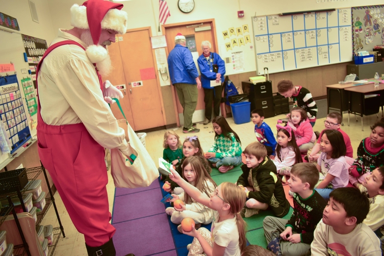 Santa Claus visits a classroom, handing out gifts to excited children.