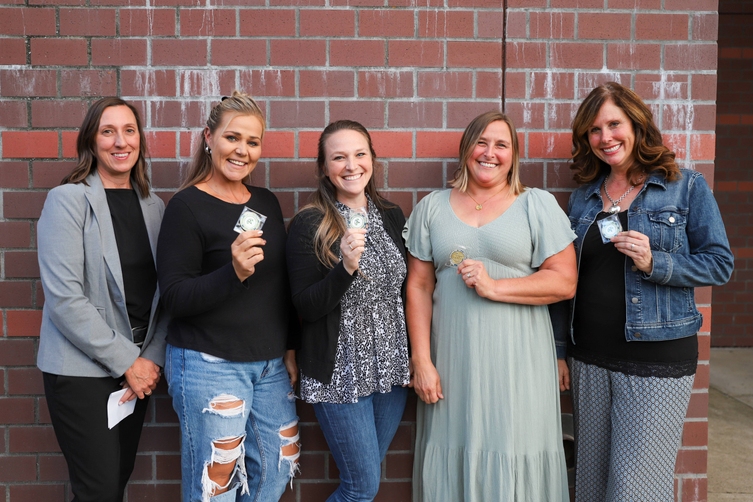 A group of 5 women stand in front of a brick wall and smileA group of 5 women stand in front of a brick wall and smile