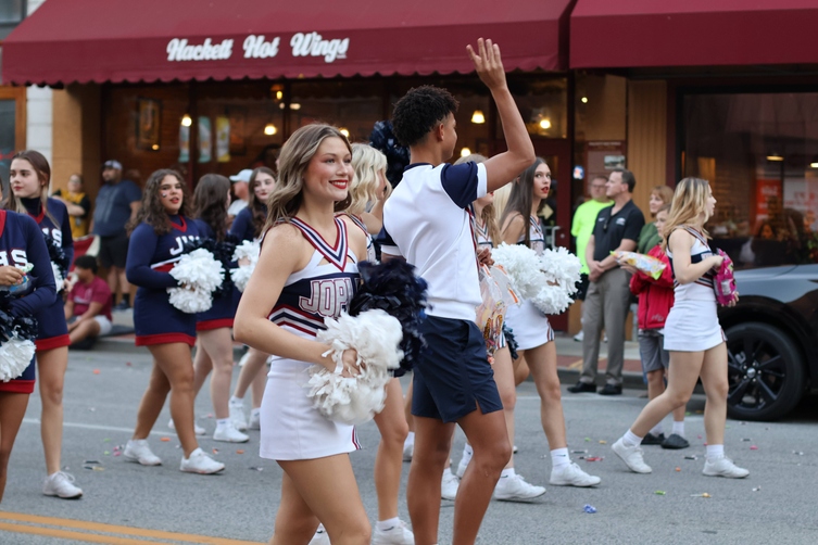 JHS Cheerleaders march in the Homecoming Parade, smiling, waving poms, and passing out candy to bystanders.