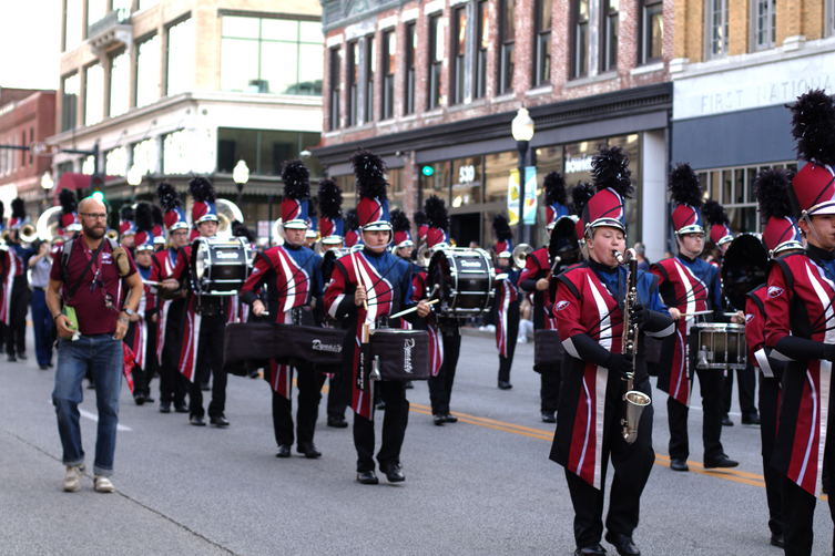 Members of the JHS Marching Band march in the parade, playing the JHS Fight Song and drum cadence, dressed in full band regalia with plumed hats.