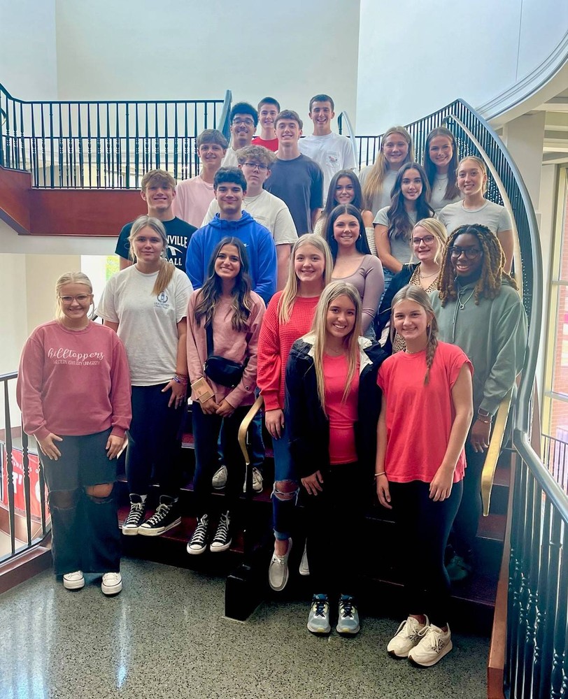 About 22 people stand on small staircase and pose for photo