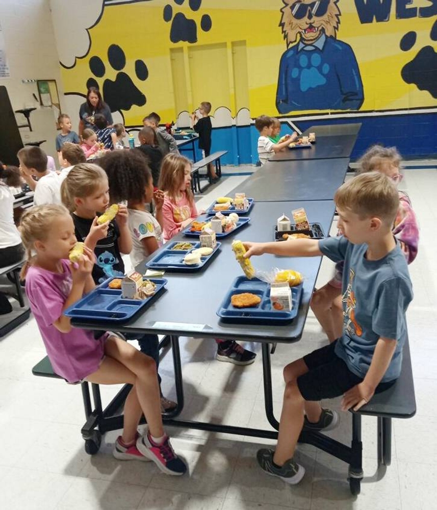 7 kids sit at cafeteria table and eat lunch