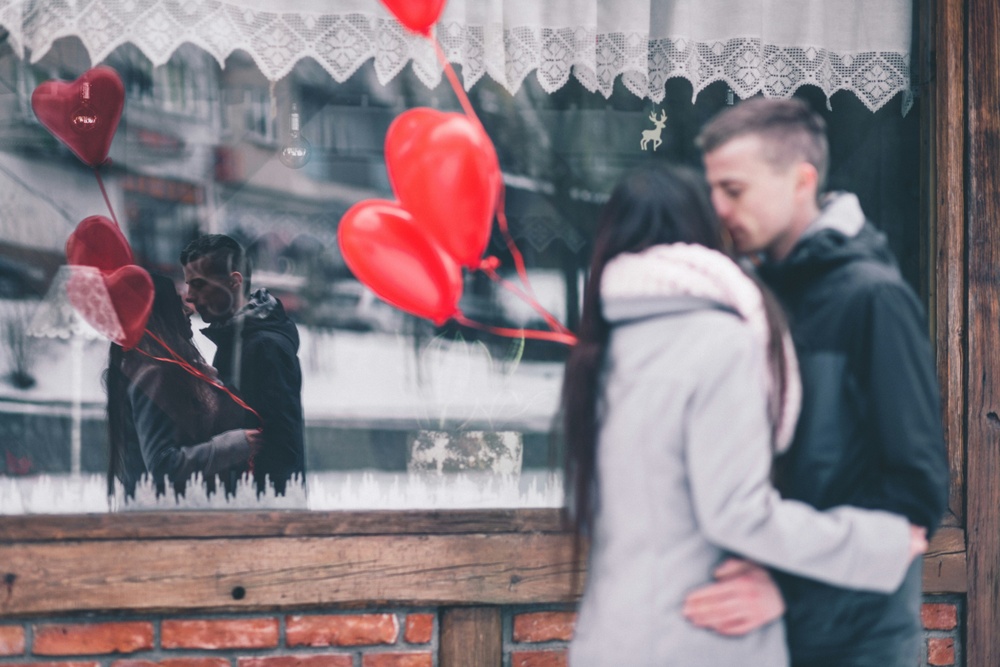 en man och en kvinna står med ballonger i form av hjärtan utanför ett skyltfönster.