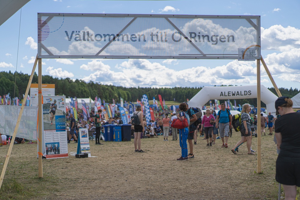 Människor och tält på gräsplätt med en banderroll med texten Välkommen till O-Ringen