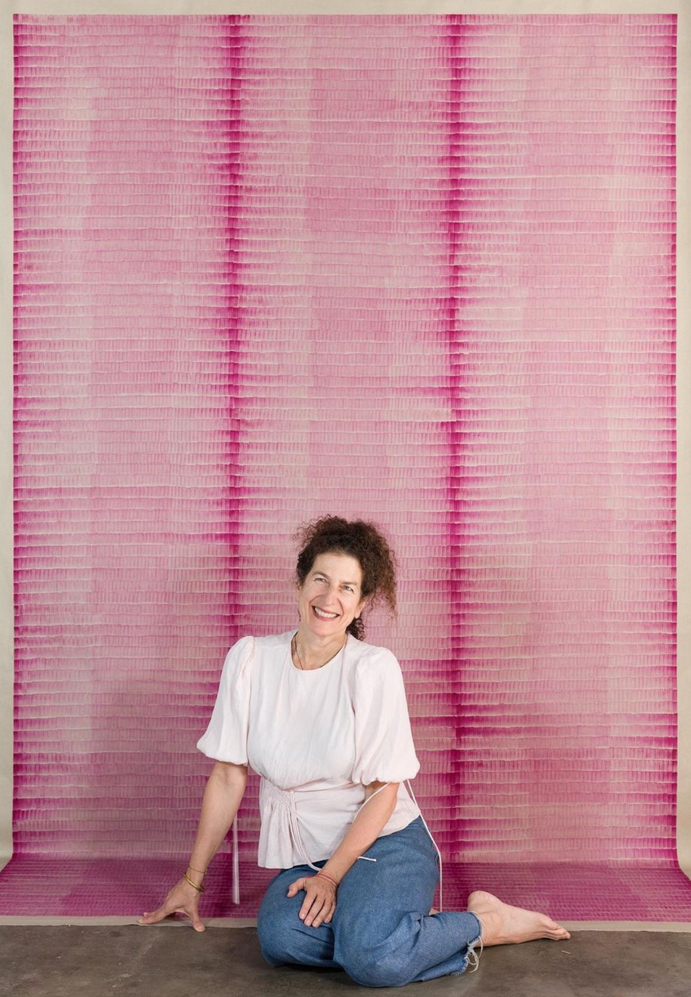 A woman sits before a wall sizes art work with a red abstact pattern.