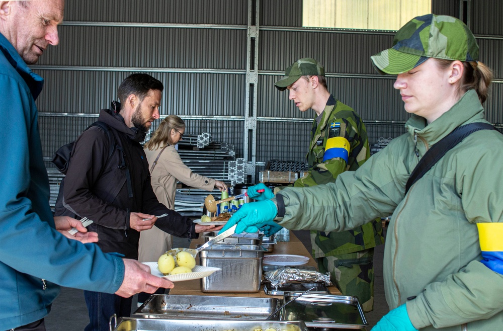 Leverans av mat är en bra övning för Lidköpings kommun eftersom Försvarsmakten ska kunna göra matbeställningar från en kommun vid höjd beredskap. Kommunikationssoldat Freja och skolinformatör Birger från F7 serverar hungriga deltagare uppskattade kåldolmar.