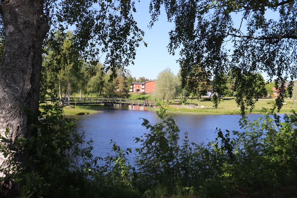 Vatten med gångbro. I bakgrunden hyreshus.