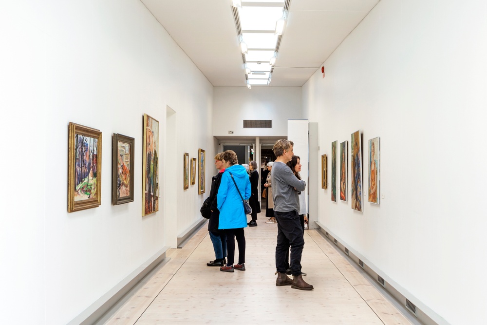 Människor betraktar upphängda konstverk i en av Bohusläns museums utställningslokaler. 