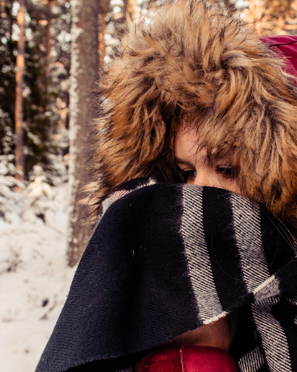 En flicka i vinterjacka i ett snölandskap, halsduken täcker ansiktet och ögonen tittar nedåt.