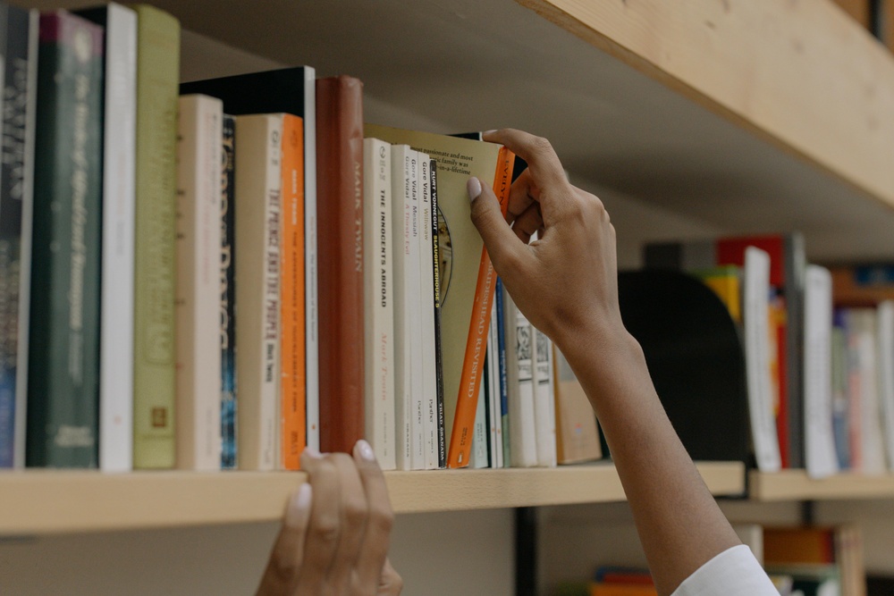 Bokhylla på bibliotek och hand som tar i en bok