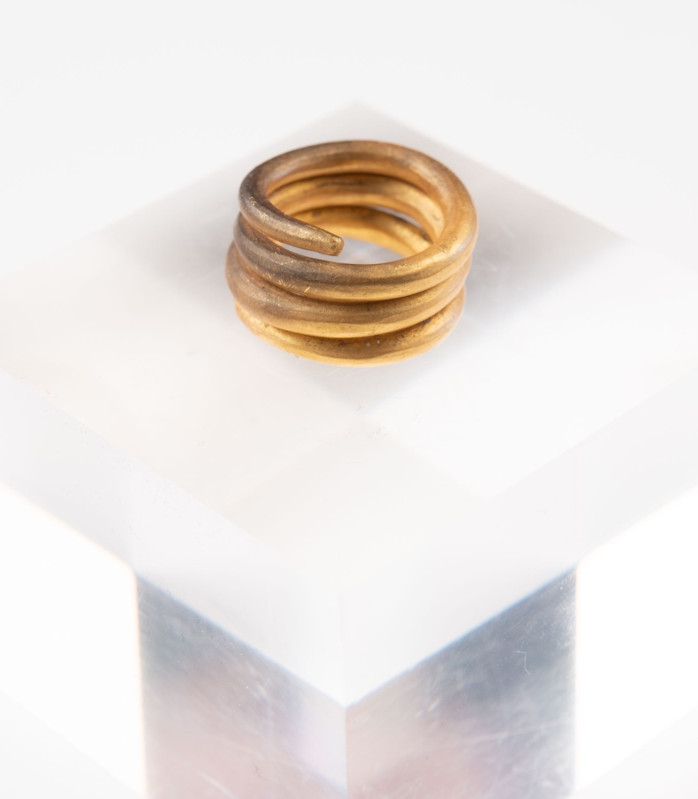 En spiralformad guldtråd i fem lager, stor nog att rymmas på ett ringfinger, vilar på en vit yta.
