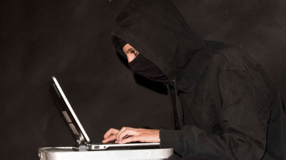 a hacker in black clothes looking intensely at the laptop 