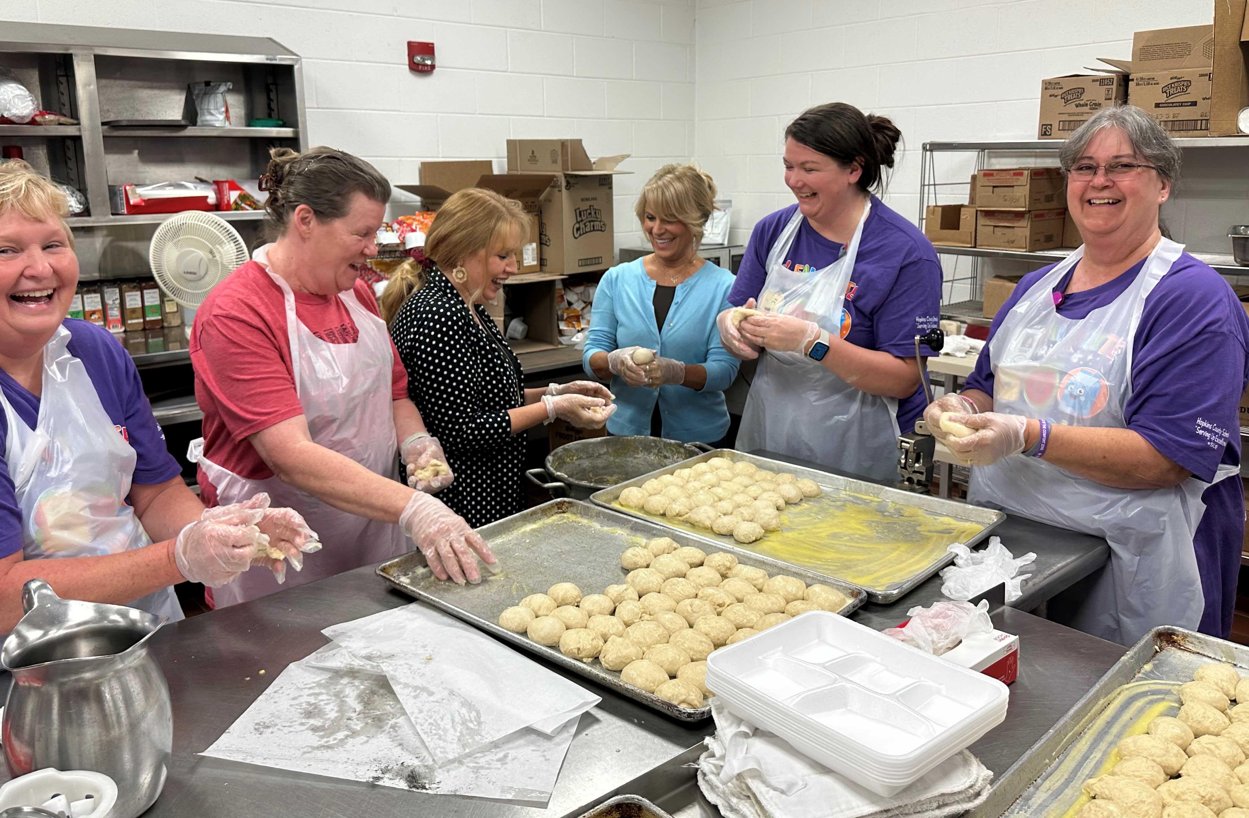 6 people wearing aprons work on roll dough