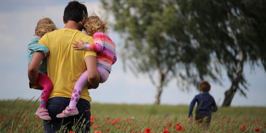 an adult carrying two children in their arms as they walk through a field of flowers